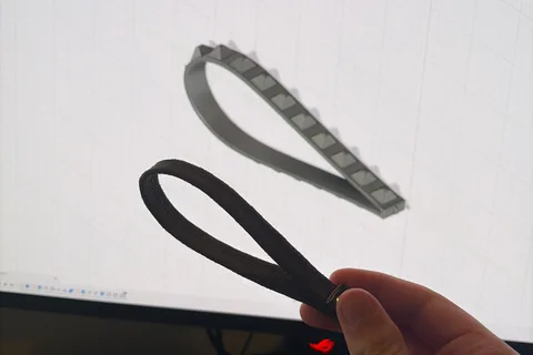 Black printed TPU wrist straps held in front of their Autodesk Fusion CAD model